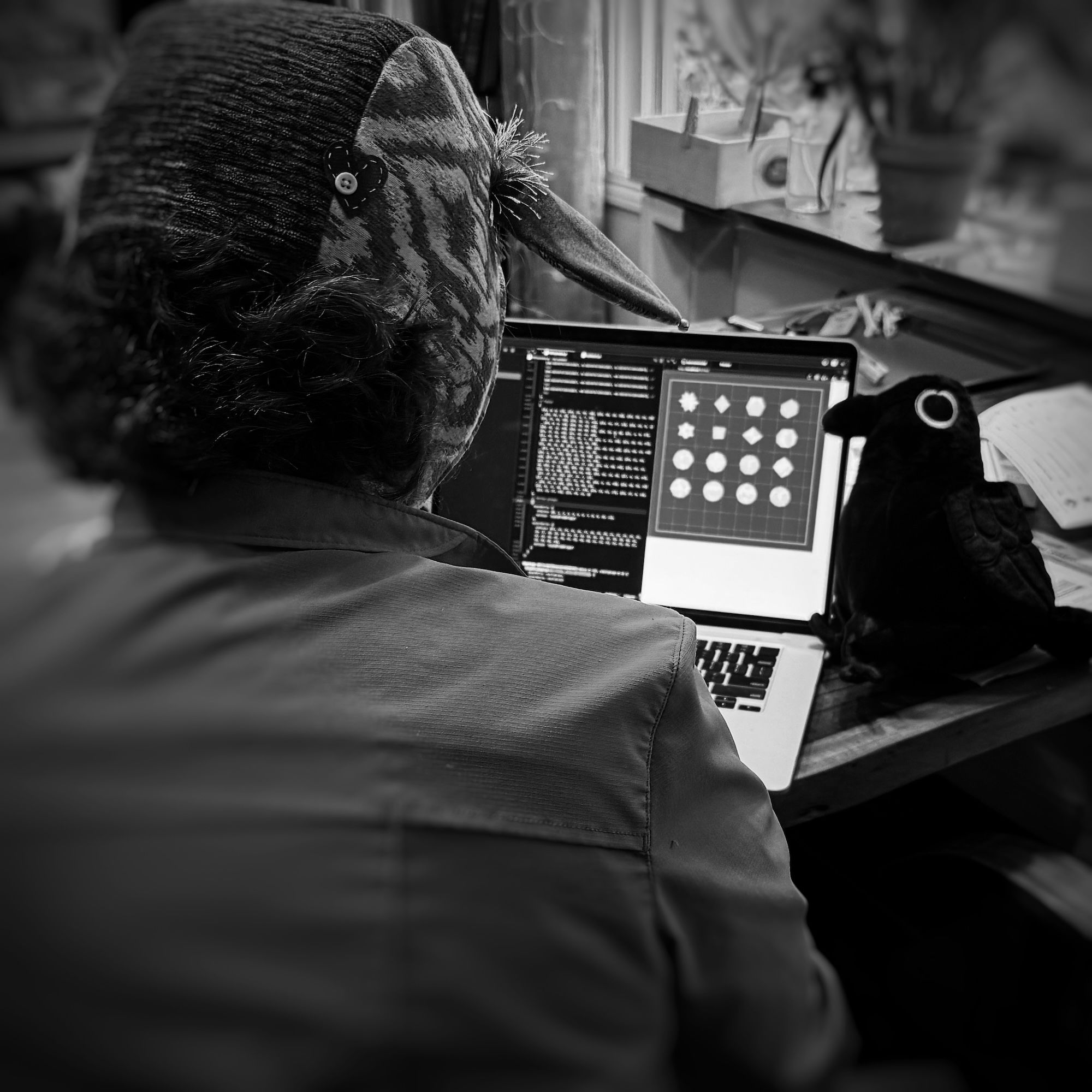 black and white of me coding in a goat hat with a crow stuffy